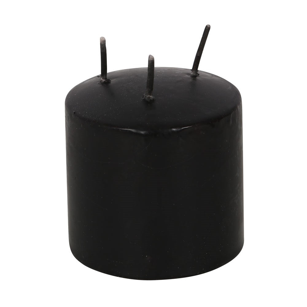 A black wax candle with dramatic red wax drips and three lit wicks, placed on a white marble surface with a dark vase and a black book in the background.