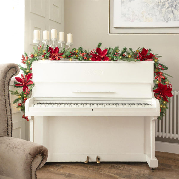 White piano decorated with Christmas garland and red bows in a room with a gray armchair.