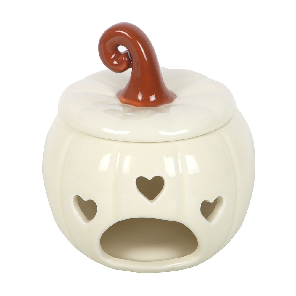 A ceramic pumpkin-shaped candle holder with a lit tea light inside, styled on a wooden surface with a vase and books in the background.