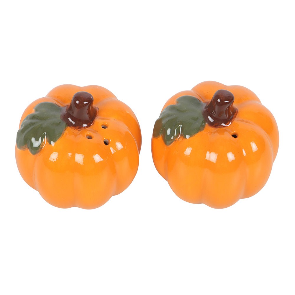 Two orange pumpkin-shaped salt and pepper shakers with green leaves and brown stems, displayed on a wooden cutting board in a kitchen setting.