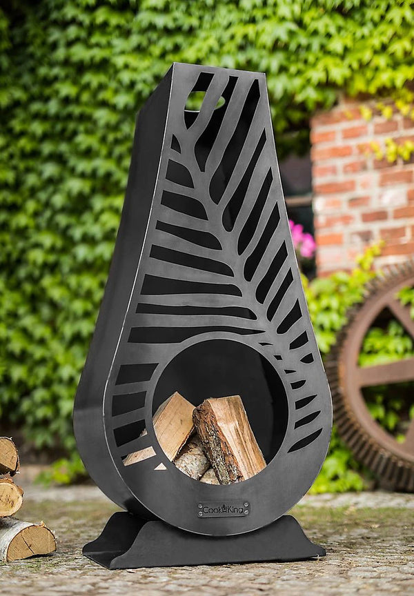 Decorative metal firewood holder with cut-out design on a garden background
