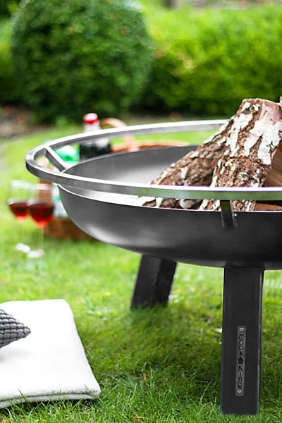 Black fire pit with logs on a grassy outdoor area