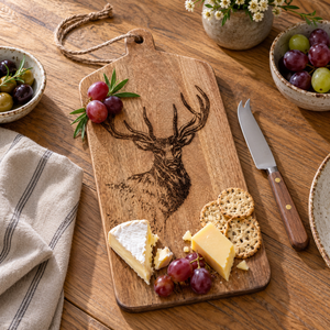 Stag engraved wooden serving board with brie, cheddar, crackers and grapes on an oak dining table.