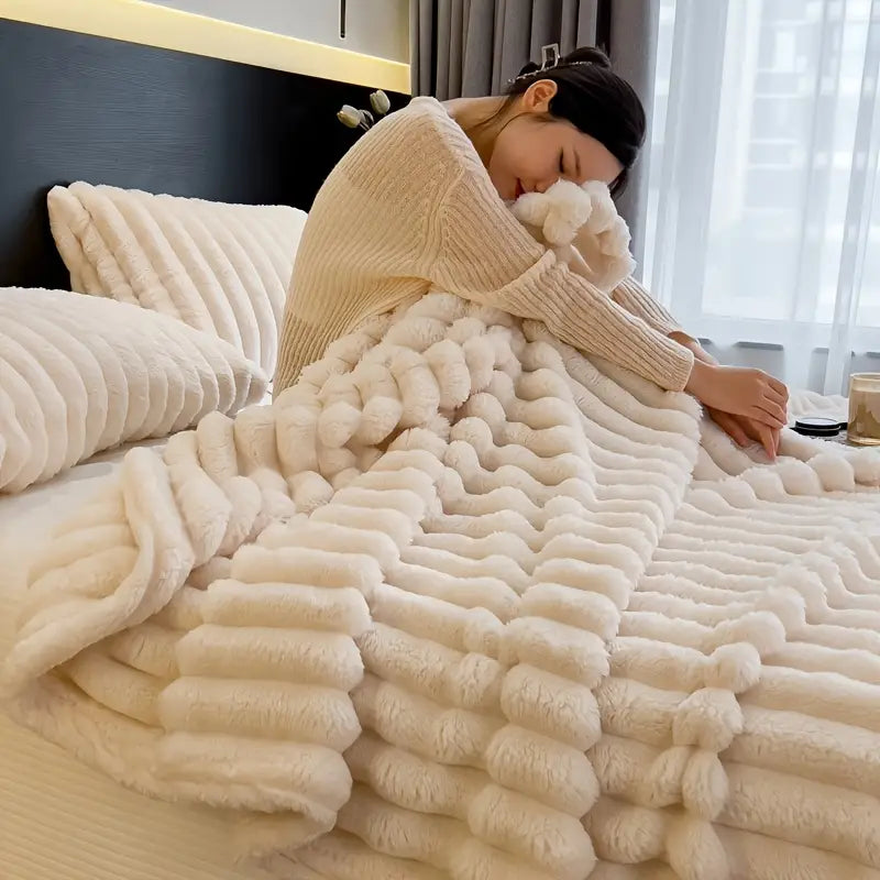 A person cuddling with a plush, faux fur throw blanket on a bed.
