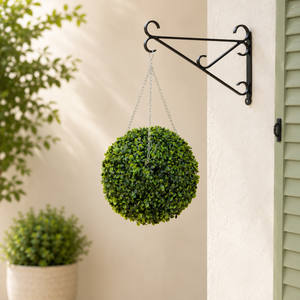Hanging green plant ball on a decorative metal bracket against a neutral wall.