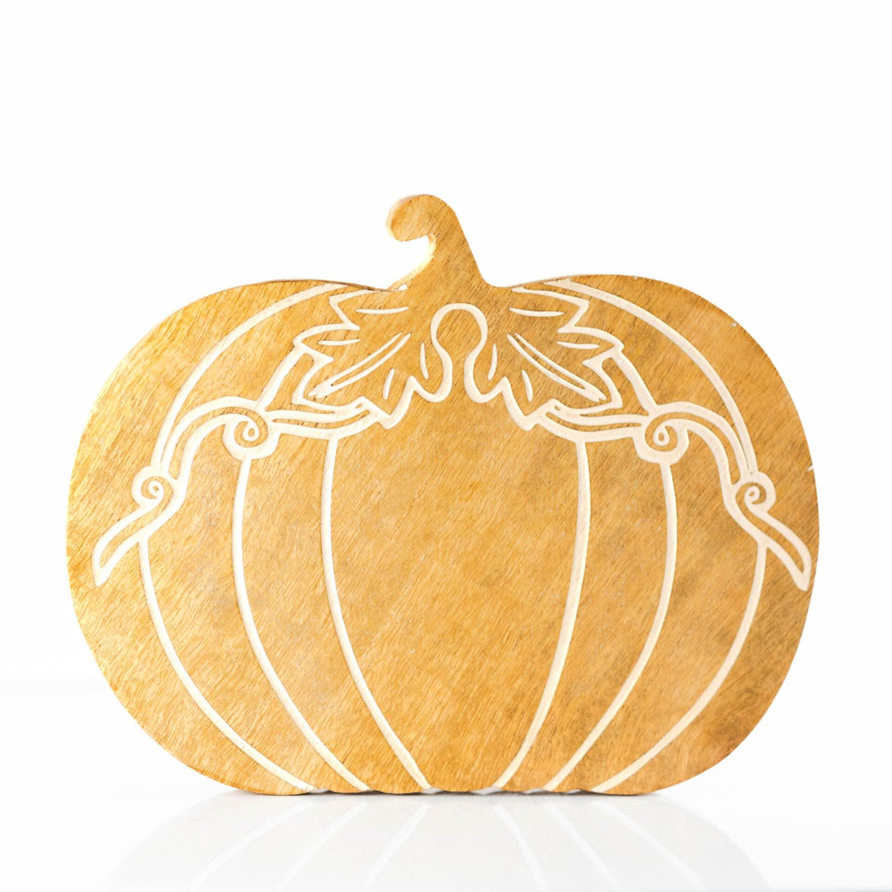 Wooden pumpkin decoration on a rustic mantelpiece beside a glass candle and autumn leaves.