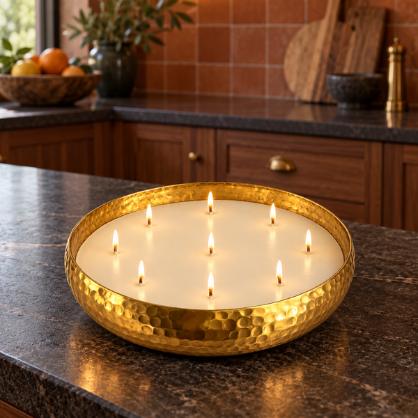 A hammered gold metal candle holder with multiple lit candles, placed on a dark granite kitchen countertop with wooden cabinets in the background.