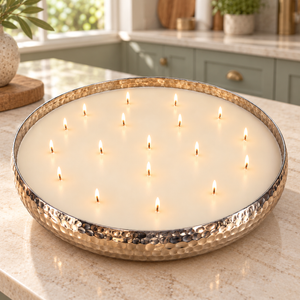 A large round wax candle in a hammered metal bowl, lit with multiple small flames, set on sage green kitchen top.