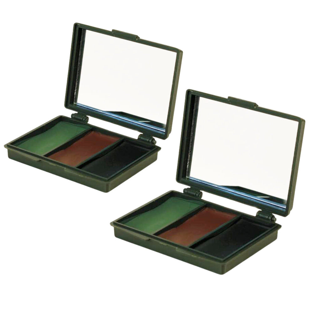 Two military-style compact powder makeup cases with mirrors, open on a rustic wooden surface outdoors. Each case contains three color pans: olive green, brown, and black.