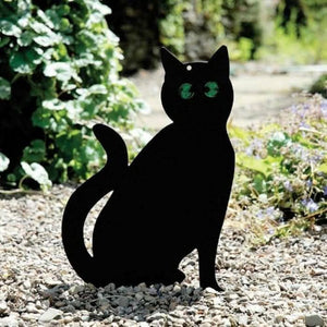 Black cat-shaped garden stake on a pebbly surface with greenery in the background