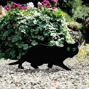 Black cat-shaped garden ornament on pebbles with flowers in the background