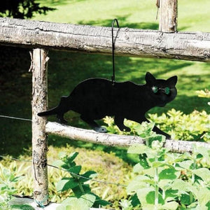 Black cat-shaped garden ornament hanging on a wooden fence with greenery in the background