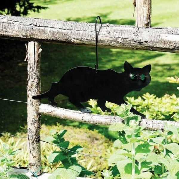 Black cat-shaped garden ornament hanging on a wooden fence with greenery in the background