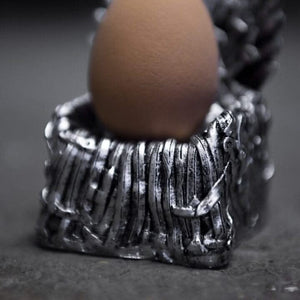 Silver egg holder with a brown egg on a dark background