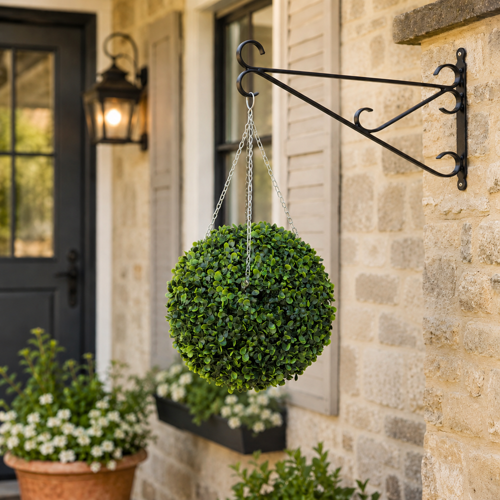 Hanging boxwood ball on a decorative bracket against a stone building exterior.