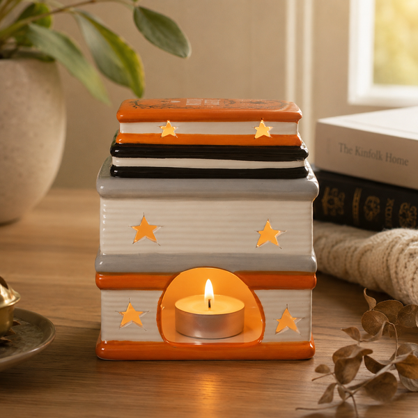 A decorative stack of books candle holder with a lit tea light candle inside, styled on a wooden table with a potted plant and books in the background.