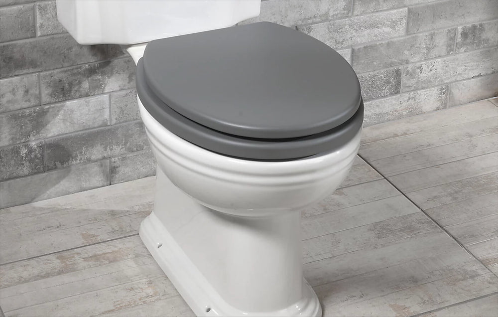 White toilet with a gray seat against a tiled bathroom wall.