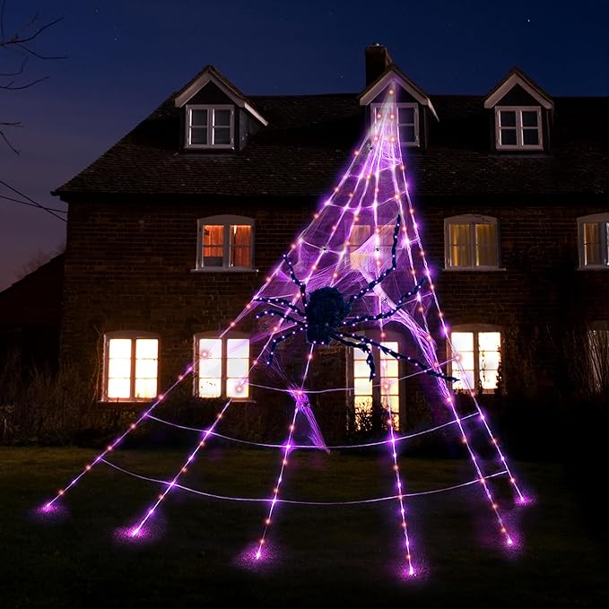 Halloween decorative spider web with a spider in front of a house at night.