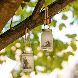Three glass jars with fairy silhouettes hanging from a tree branch.