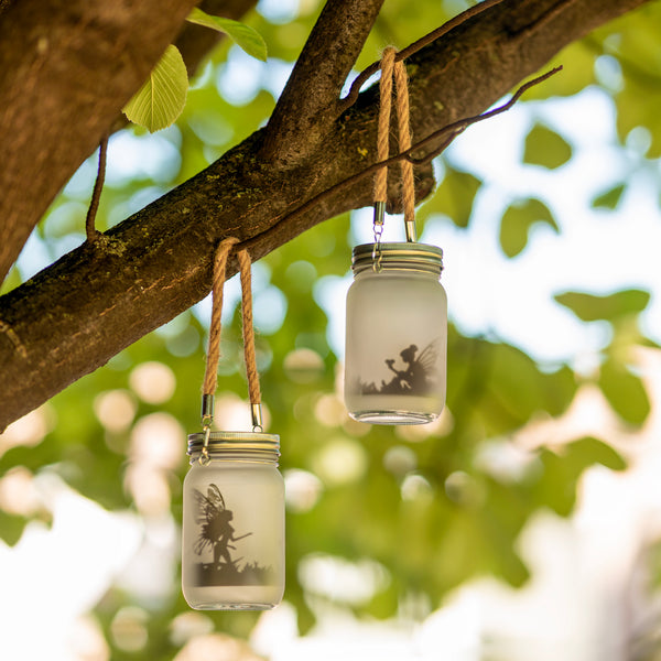 Three glass jars with fairy silhouettes hanging from a tree branch.