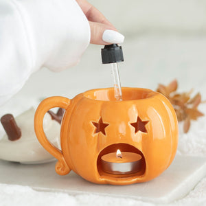 Pumpkin-shaped candle holder with a lit tealight and a hand using a dropper.