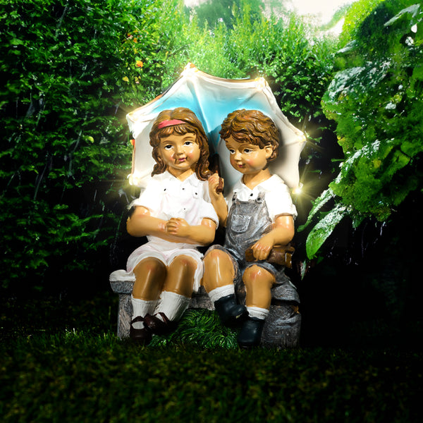 Resin children sitting beneath illuminated umbrella