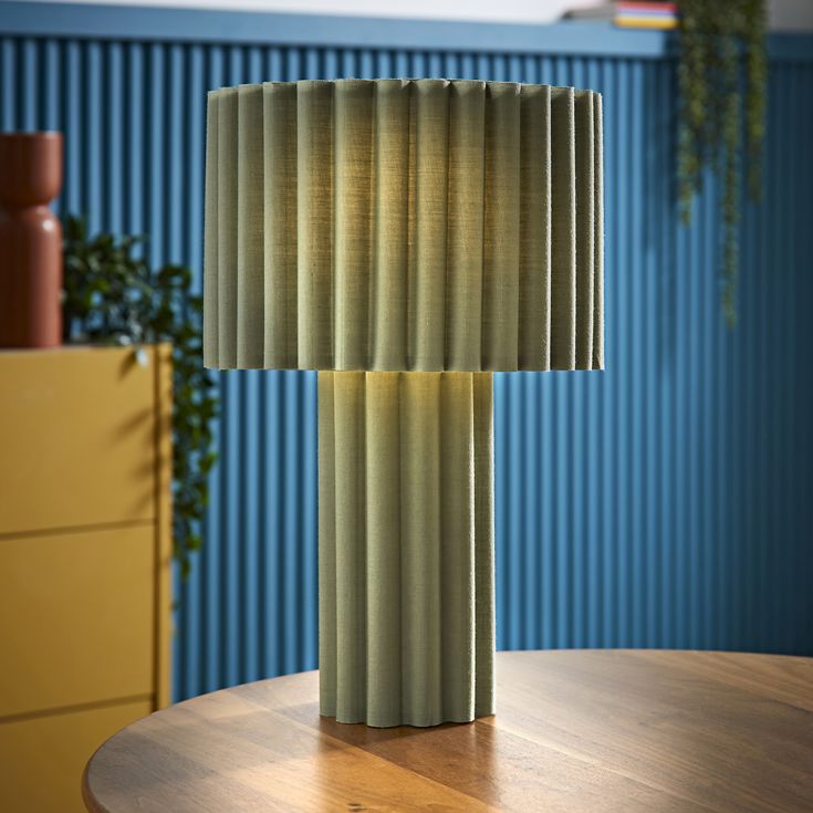 Green pleated lamp on a wooden table with a blue wall and yellow cabinet in the background