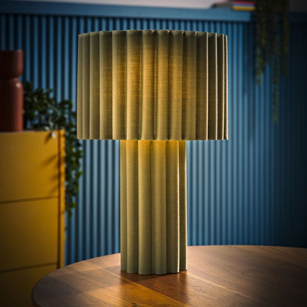 Decorative lamp with pleated design on a wooden table against a blue wall.