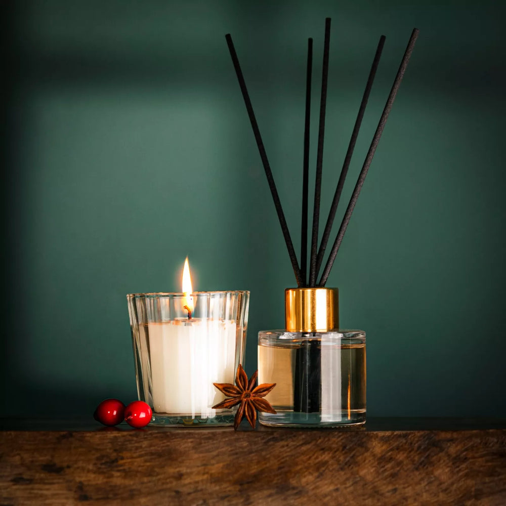 Candle and diffuser with anise star on a wooden surface against a green background