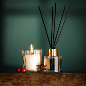 Candle and diffuser with anise star on a wooden surface against a green background