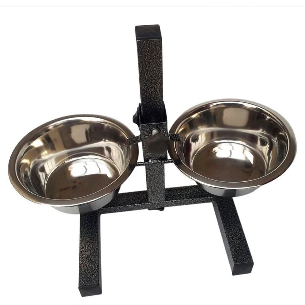 A black automatic pet feeder with two stainless steel bowls on a wooden kitchen floor, with one bowl filled with dry dog food and the other empty water bowl. The background shows a modern kitchen with light wood floors and cream-colored cabinets.
