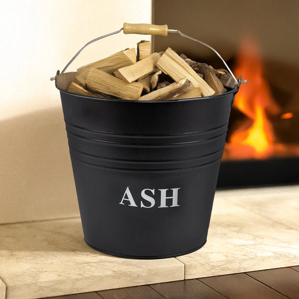 Black bucket labeled 'ASH' filled with wooden logs in front of a fireplace.