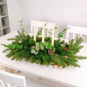 Decorative table centerpiece with greenery and candles on a white table.