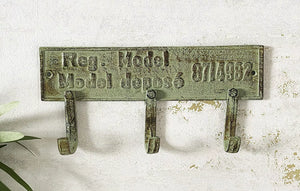 Vintage-style metal wall hook with engraved text on a textured white background