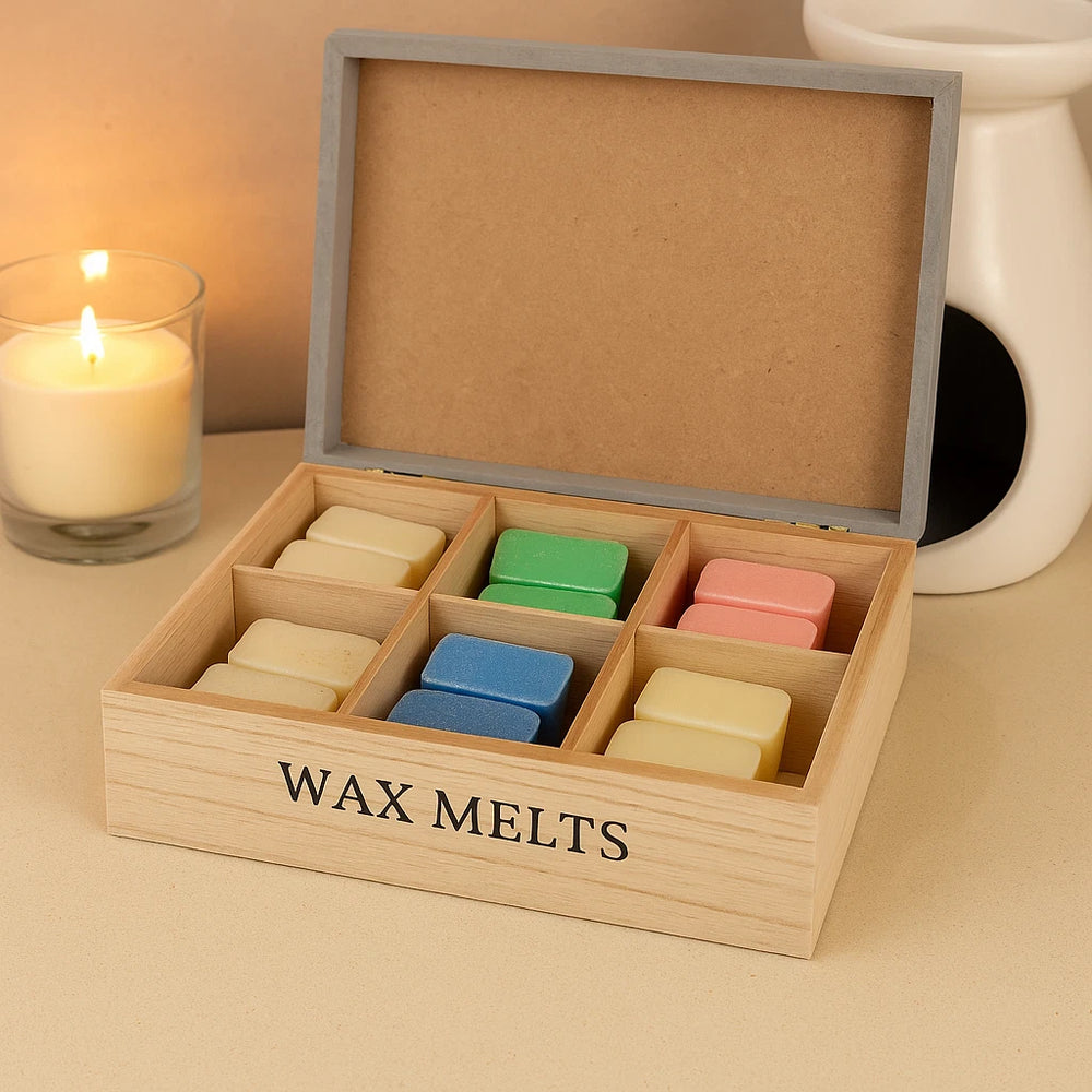 Wooden box of wax melts with colorful wax melts inside, on a table with a candle in the background.