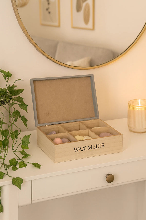 Wooden box labeled 'Wax Melts' on a table with a mirror and plant in the background