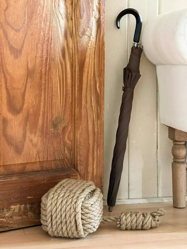 Brown umbrella leaning against a wooden wall with a rope roll on the floor.