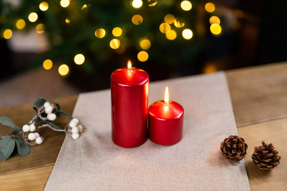 Two red candles on a table with blurred Christmas lights in the background