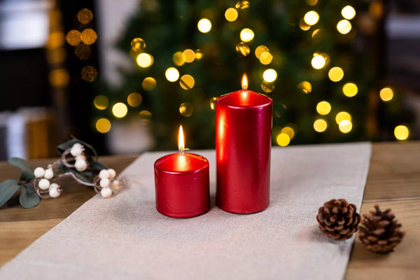 Two red candles on a table with a blurred Christmas tree in the background