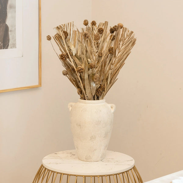 Decorative vase with dried plants on a marble table against a beige wall.