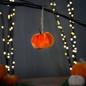 Decorative orange pumpkin hanging from a branch with blurred lights in the background