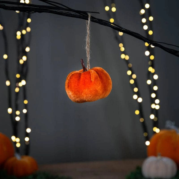 Decorative orange pumpkin hanging from a branch with blurred lights in the background