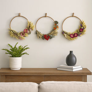 Three decorative wreaths on a wall above a wooden console table with a plant and vases.