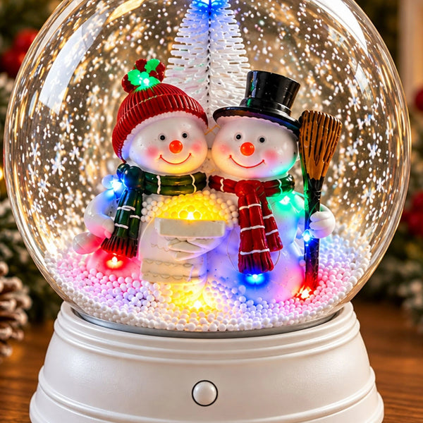 A festive snow globe decoration with two smiling snowman figures inside. One snowman wears a red hat and green scarf, and the other wears a black top hat and red scarf.