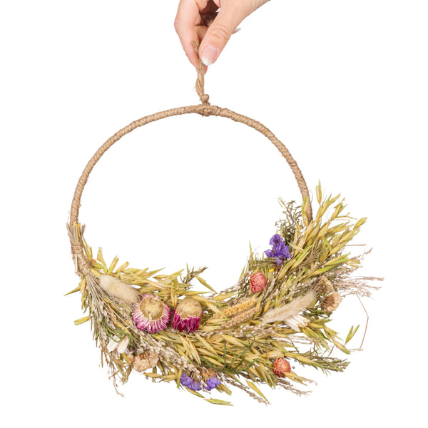 Hand holding a decorative wreath with natural elements on a white background