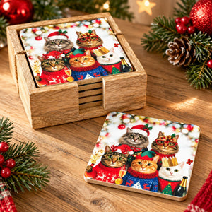 A set of square wooden coasters with a festive Christmas print of four cats in holiday sweaters, shown with one coaster standing in a matching wooden box and another lying flat on a wooden table surrounded by holiday greenery and red ornaments.