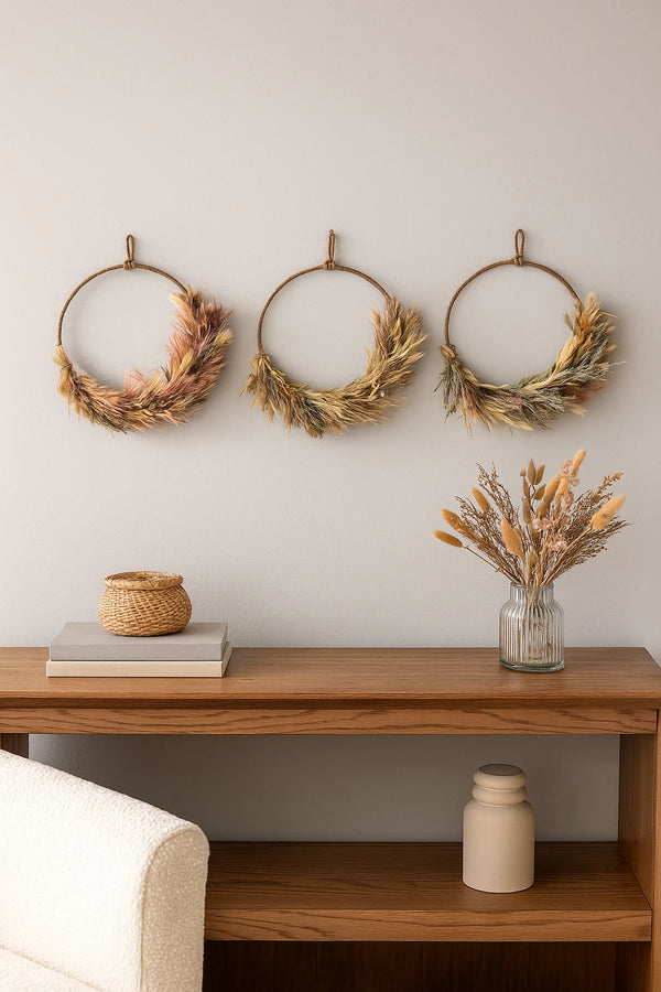 Three decorative wreaths on a wall above a wooden console table with a vase and books.