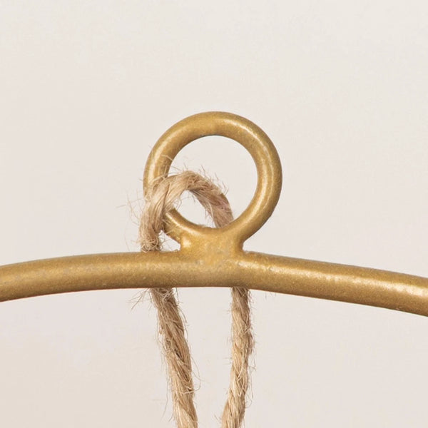 Gold metal hanger with a piece of twine on a beige background