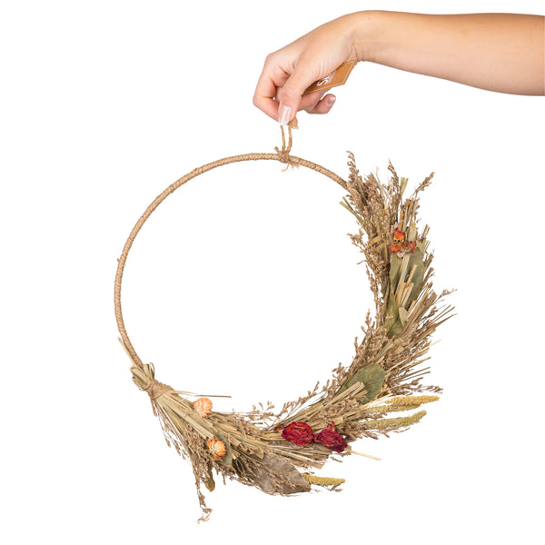 Hand holding a dried wreath with natural elements on a white background