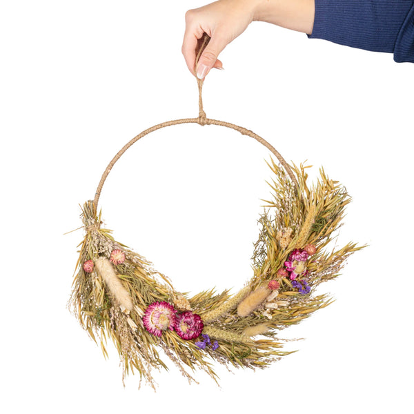 Hand holding a dried wreath with flowers on a white background